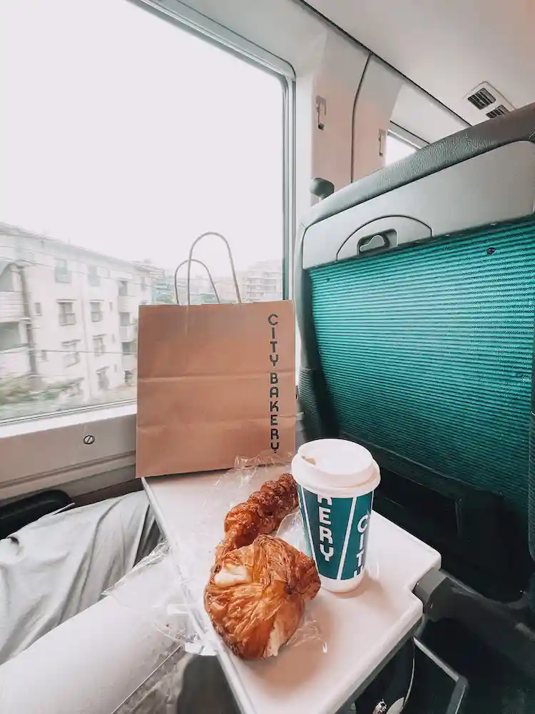 A table on a train with a bag, two pastries and a coffee cup