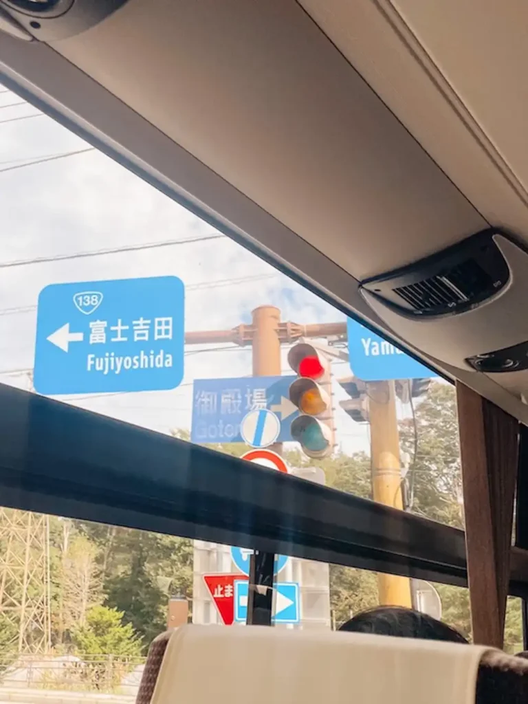 A window on a bus with three blue road signs and a traffic light outside