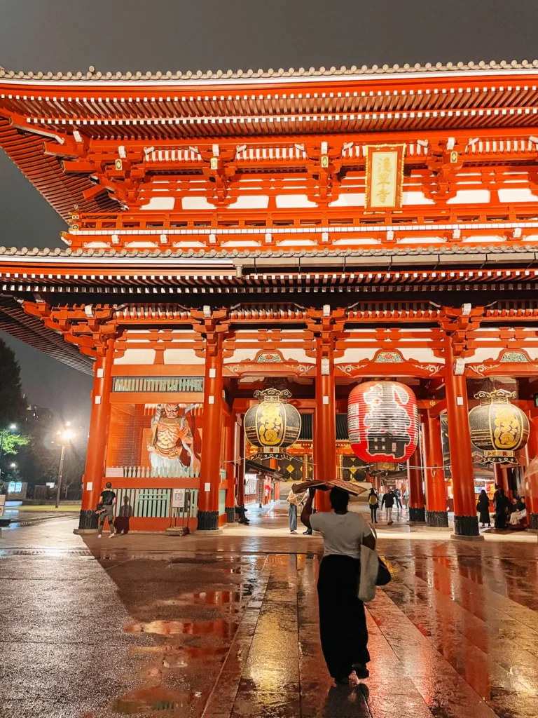 A woman standing in front of the gates at Senso-ji Temple at night time.