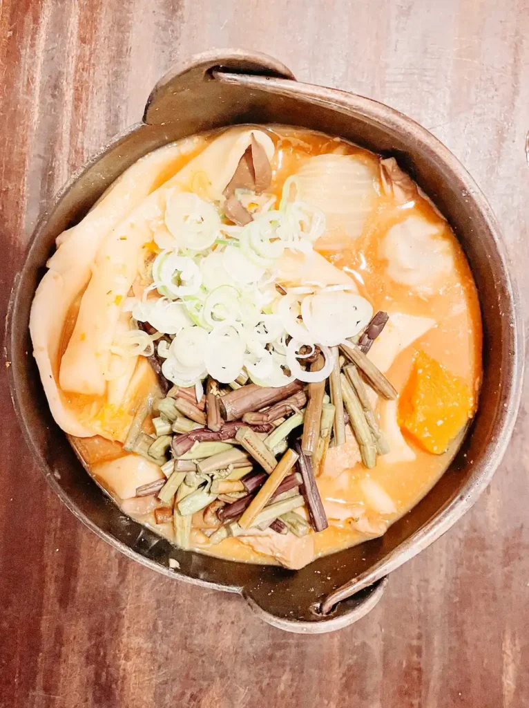 A bowl of thick noodles in a soupy pumpkin broth on a wooden table at Kosaku, Lake Yamanaka.