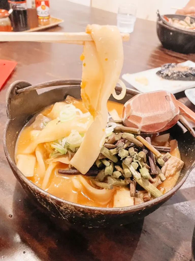 A bowl of thick noodles in a soupy pumpkin broth on a wooden table at Kosaku, Lake Yamanaka.