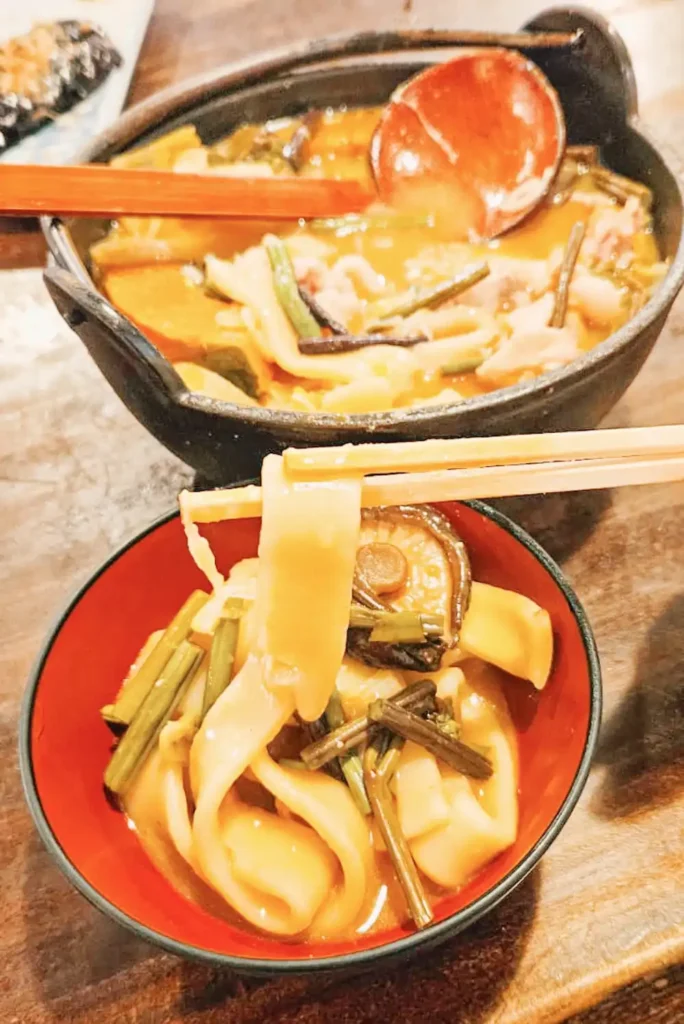 A bowl of thick noodles in a soupy pumpkin broth on a wooden table at Kosaku, Lake Yamanaka.