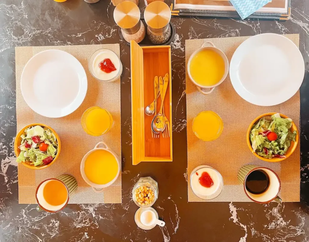 A birds eye view of two breakfast boards on a table consisting of juice, yoghurt, soup and salad