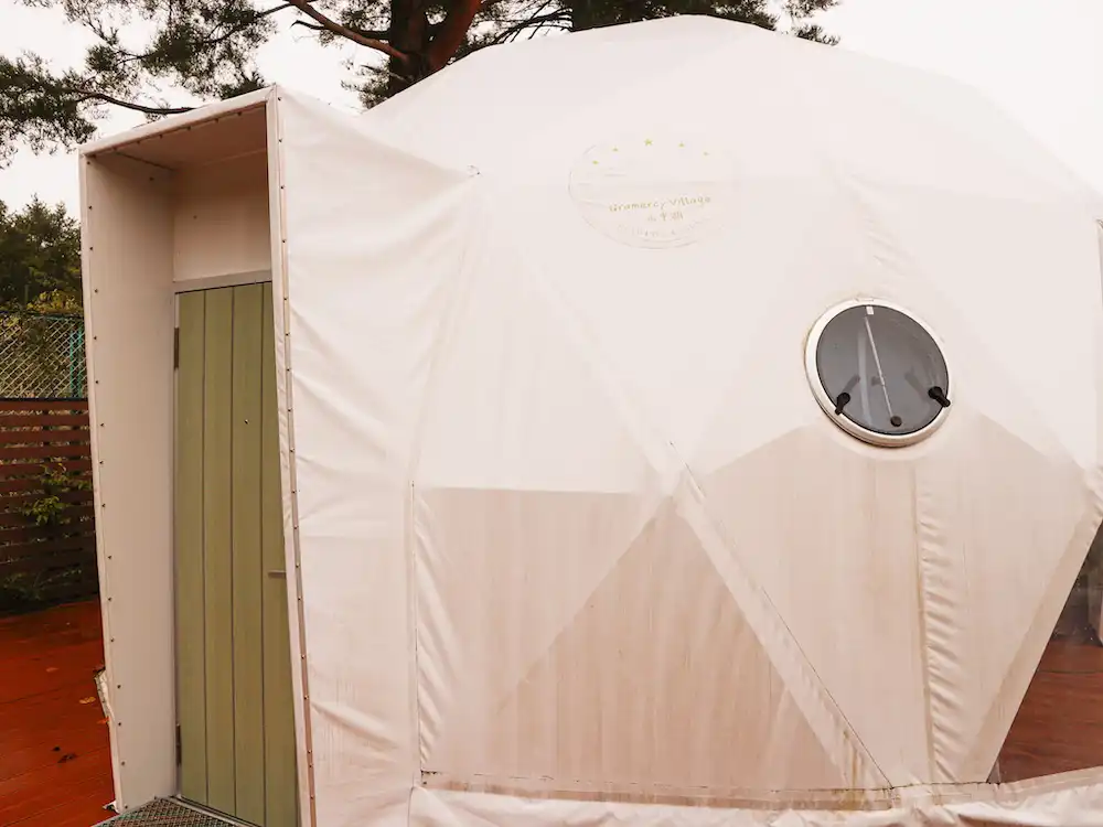 The exterior of a white glamping dome with a green door