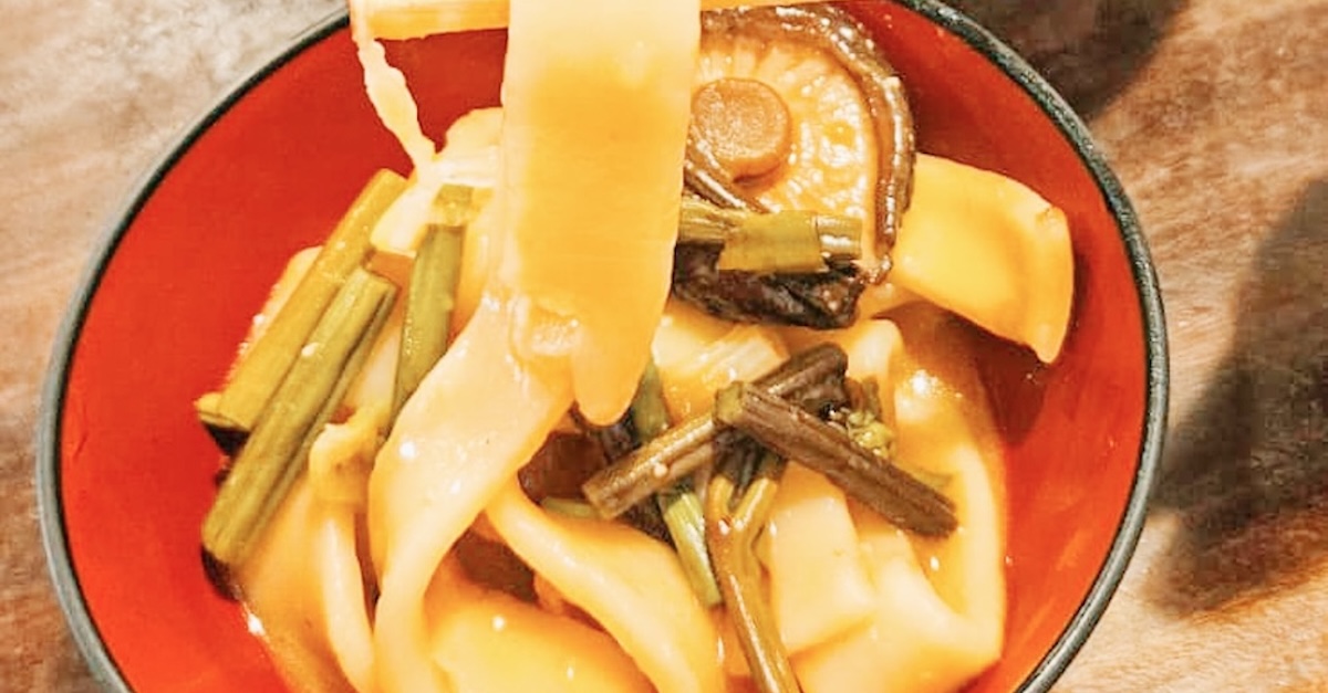 A bowl of thick noodles in a soupy pumpkin broth on a wooden table at Kosaku, Lake Yamanaka.