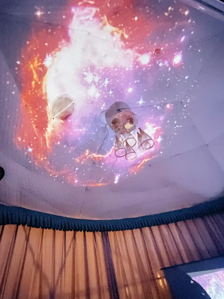 The interior of a tent with a purple and red galaxy projected on the roof.