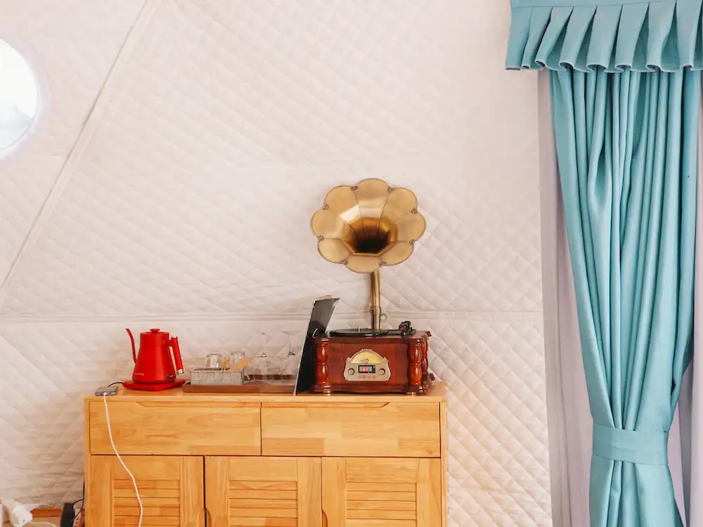 A wooden console with a red kettle, coffee and Bluetooth gramophone speaker on top of it