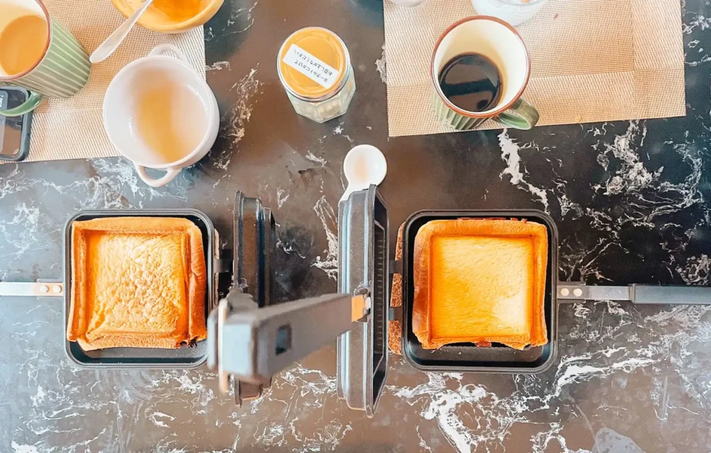 Two grilled cheese toasties on a table next to cups of coffee and juice